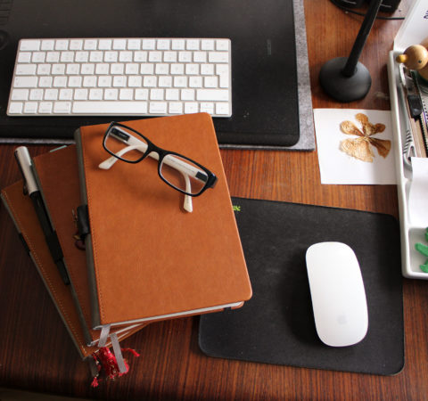 My Bujos are just about to get better with Tap Forms 5 Photo © Kimberley Hoffman 3 stacked bullet journals on dark wooden desk. Mac mouse and keyboard, Wacom Intuos Pro Paper, pressed flower