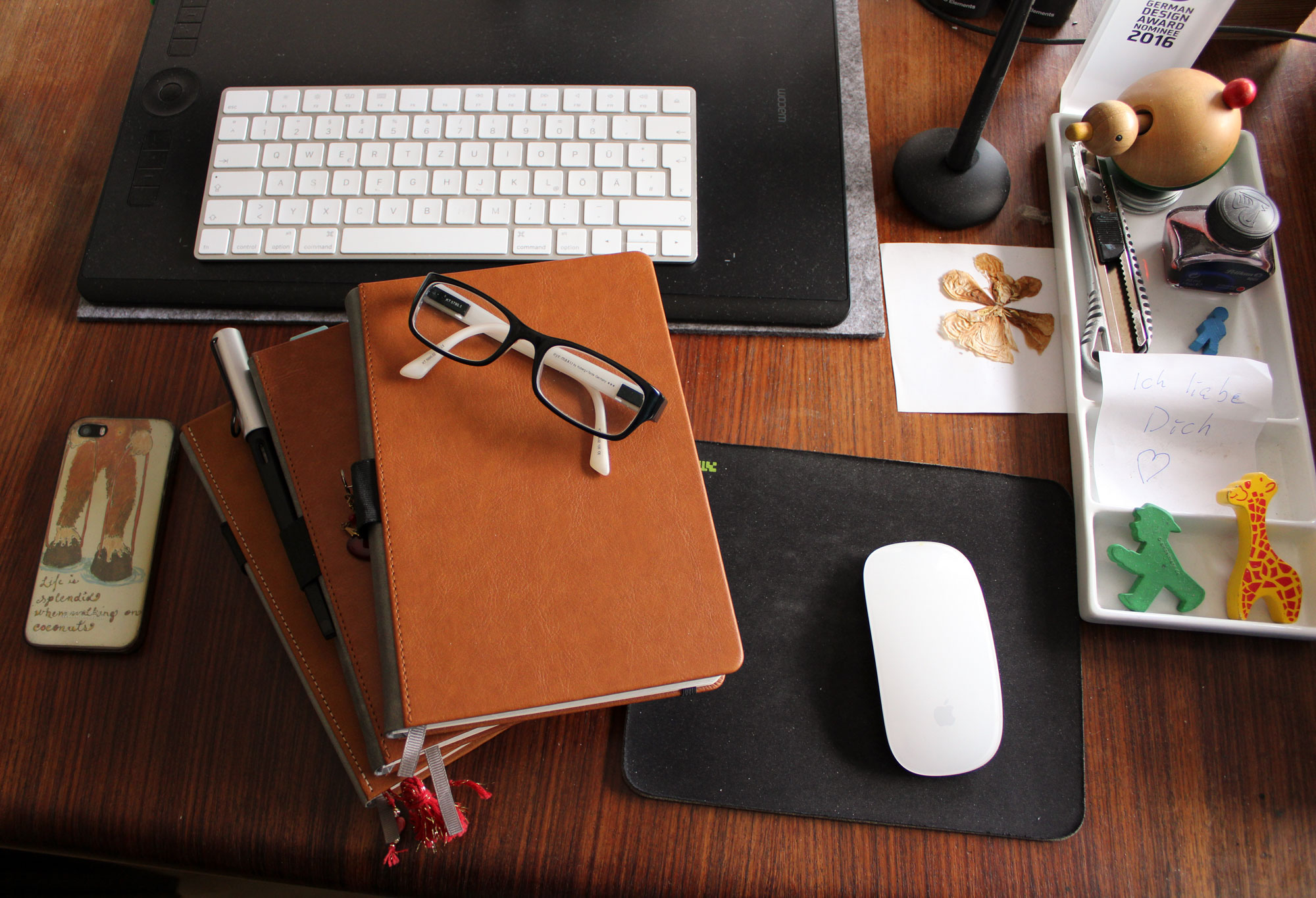 My Bujos are just about to get better with Tap Forms 5 Photo © Kimberley Hoffman 3 stacked bullet journals on dark wooden desk. Mac mouse and keyboard, Wacom Intuos Pro Paper, pressed flower