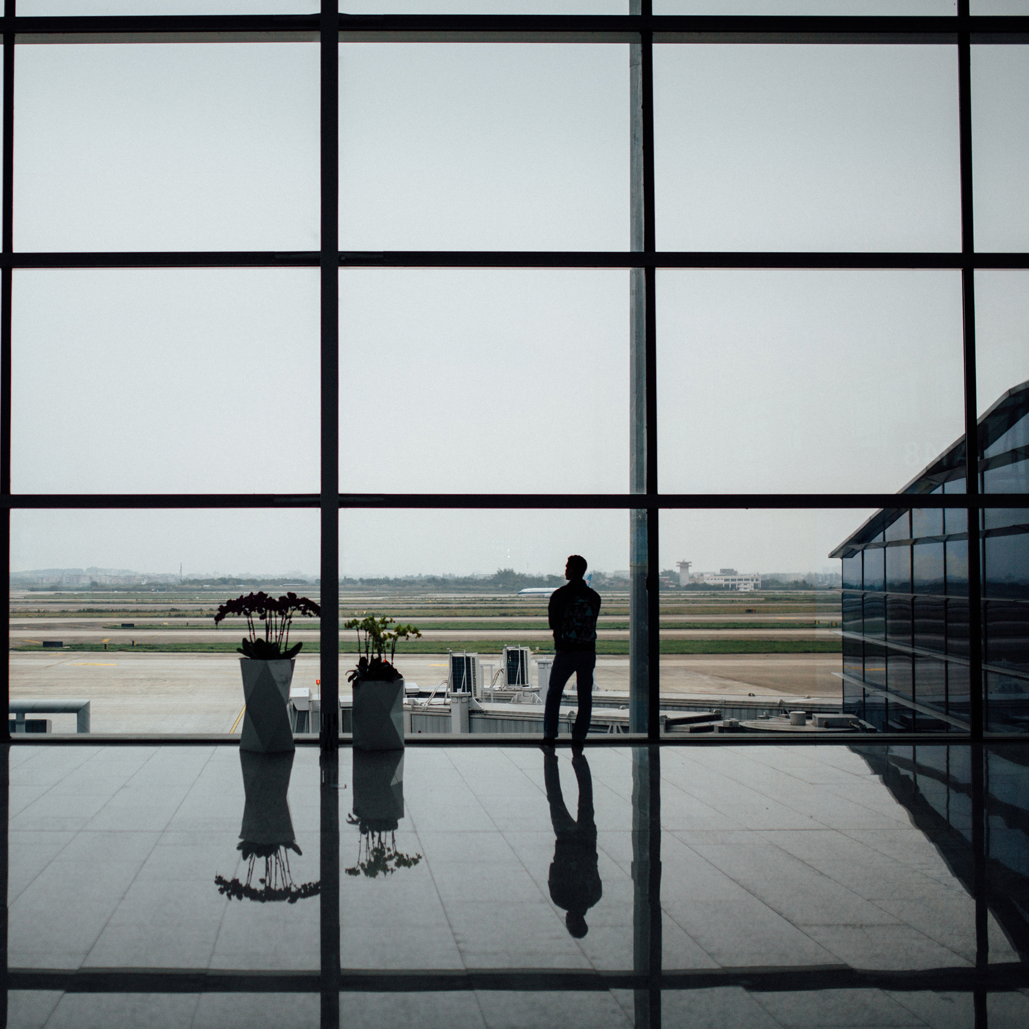 Foto von Hanson lu am Unsplash Das Beste zum Schluss: Foto eines Menschens, der am Flughafen einsam und allein auf etwas wartet. Er schaut durch die große Fensterscheiben auf die Landebahn.
