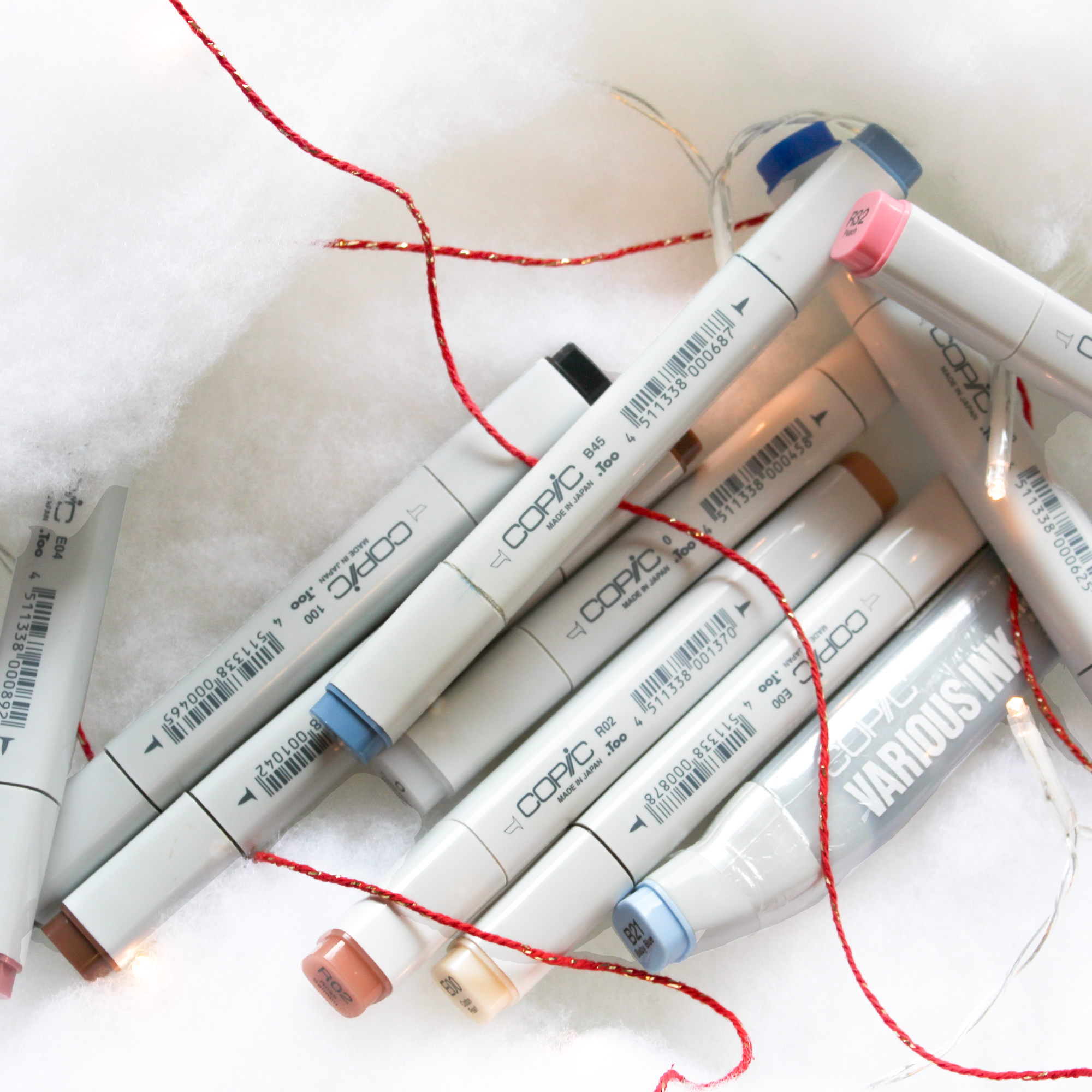 20191212 10 Presents Copic Markers Photo ©Kimberley Hoffman www.hoffman-illustrates.com Shows a variety of Copic brand markers on a white fluffy background with red twine and blinking lights around them.