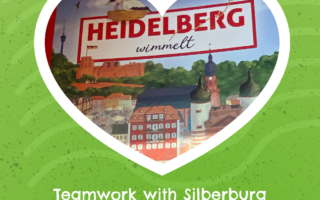 Front page of "Heidelberg wimmelt", framed with a white heart. The background is green. The caption reads: Teamwork with Silberburg launchen »Teeming in Heidelberg«.